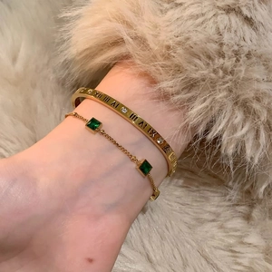 Gold tone Roman numeral bangle and emerald sugar cube bracelet set on woman wrist