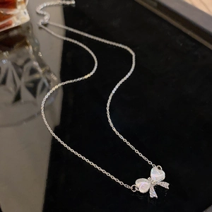 Dettaglio ravvicinato di una collana a fiocco in argento con zirconi su superficie riflettente