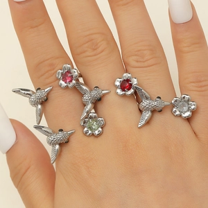 Vintage floral and hummingbird rings set with colorful crystals worn on a hand