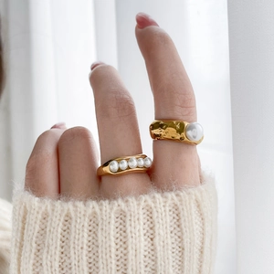 Detail of gold pea-shaped rings with freshwater pearls on hand against a knit sweater