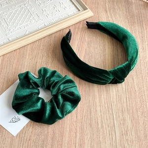 Close-up of a dark green velvet headband and matching scrunchie on a wooden surface