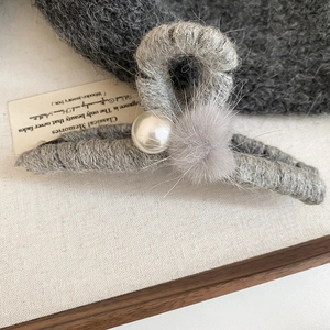 Nahaufnahme einer grauen gestrickten Haarklammer mit weißen Perlen und weichen Plüschpompons