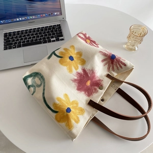 Detail of canvas tote bag with floral print and leather handles next to a laptop