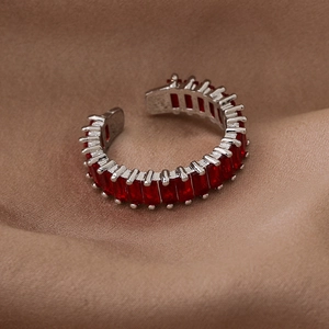 Macro shot of silver open ring with red emerald-cut zircon on brown silk fabric