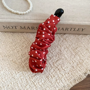Détail de la pince banane rouge à pois en satin sur fond de style vintage
