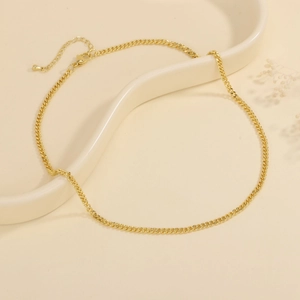 Detail of a 18K gold plated Cuban link necklace with lobster clasp on a beige tray
