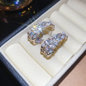 Detailed view of C-shaped earrings with faux pearls and crystals in a velvet jewelry box