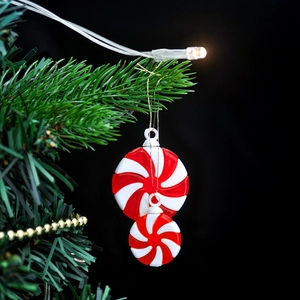 Red and white peppermint candy Christmas ornaments hanging on a green festive tree branch