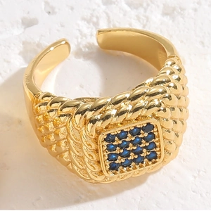 Detail of gold woven band ring featuring square blue zircon gemstones on white background