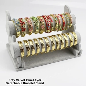 Detail of 2-tier grey velvet stand showcasing gold bangles and enamel bracelets