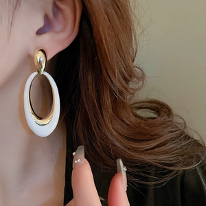 Close-up of elegant oversized oval enamel drop earrings worn by a model in white and gold