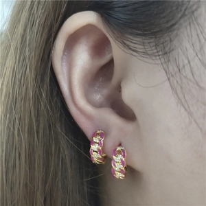 Close-up of gold chain earrings with pink enamel and white zircon on female ear