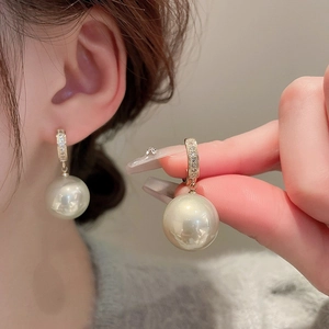 Detail of gold pearl earrings with micro-inlaid crystals worn on the ear model