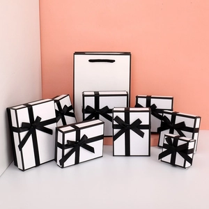 Multiple sizes of white luxury gift boxes with black ribbons and matching paper tote bag