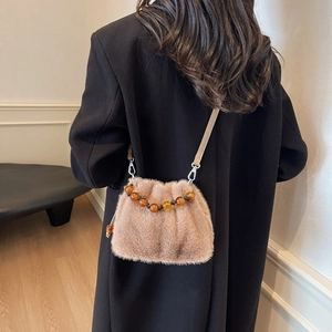Khaki plush bucket bag with amber bead handle worn by model over a black coat