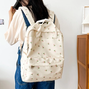 Floral backpack with pink roses detail shown on a model in a cozy indoor setting