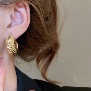 Detail of chunky gold C-shaped hoop earrings featuring a textured granulated finish on model