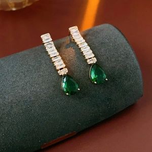 Detailed shot of gold drop earrings with green teardrop stones and rectangle zircon crystals