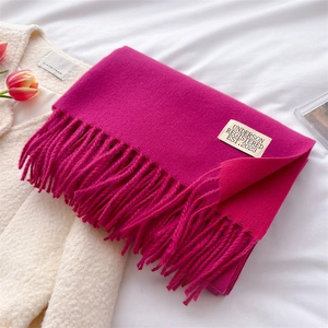 Detail of rose red cashmere feel scarf with long tassels and stylish woven brand label