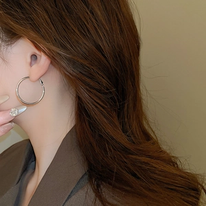 Close-up of a model wearing large silver round hoop earrings with polished metal finish