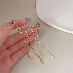 Detail of gold and silver S925 Figaro bracelets held by hand against neutral background