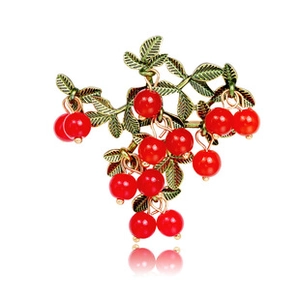 Detailed close-up of vintage metal brooch featuring vibrant red berries and green leaves