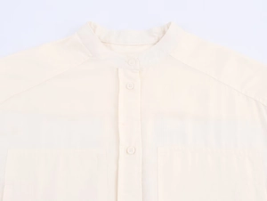 Détail d'une chemise crème à col montant avec boutons en résine et grandes poches
