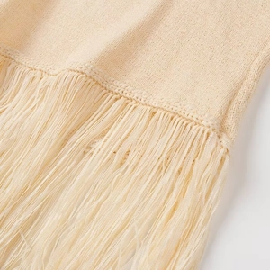 Dettaglio della trama in maglia beige con nappe a frangia e motivi intrecciati rifiniti