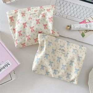 Detail of floral bow canvas cosmetic bags with zipper closure and woven label on white desk