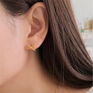 Macro shot of gold bow stud earrings with twisted rope texture on a model's ear