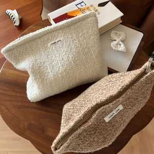 Detail showing two textured tweed cosmetic bags in beige and brown with zipper closure