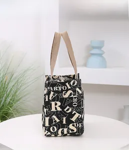 Vue détaillée du sac isotherme en toile noire avec motif lettres beiges sur table blanche