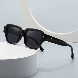 Modern square black oversized sunglasses with gold metal accent on a minimalist pedestal