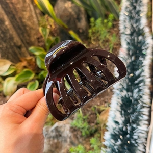 Macro detail of a glossy dark reddish-brown resin hair claw clip held outdoors