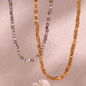 Detailed close-up of 18K gold and silver plated cube bead necklaces on textured background