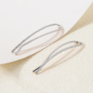 Detail view of wave-shaped silver earrings on minimalist white textured background