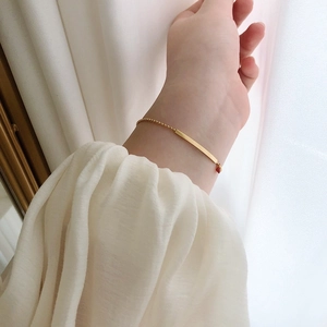 Detail of a minimalist gold bead chain bracelet with a polished bar and a tiny red heart