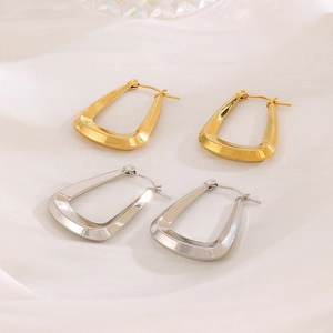 Detailed view of geometric C-shaped hoop earrings in gold and silver on white silk
