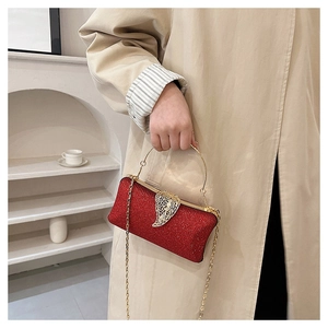 Red glitter evening clutch bag with golden leaf clasp and metal handle on a beige trench coat