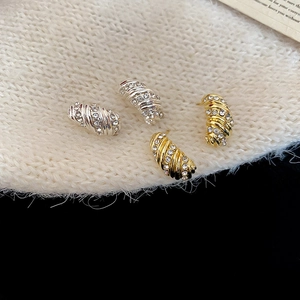 Macro shot of gold and silver spiral stud earrings with crystals on a knit background