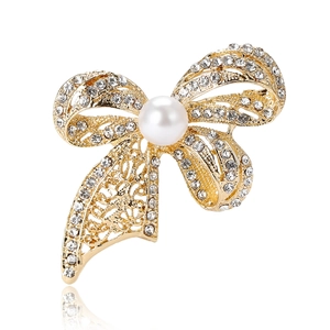Vintage gold bow brooch with sparkling rhinestones and a white pearl on white background