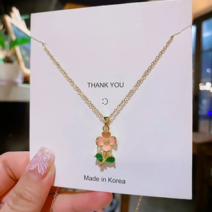 Minimalist gold titanium necklace featuring a delicate pink flower pendant and green leaves