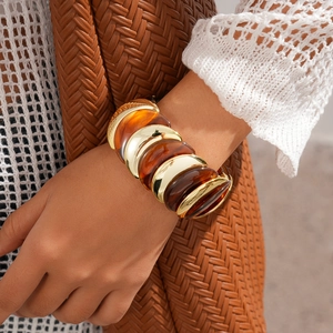 Dettaglio macro del bracciale a segmenti in acrilico ambra e metallo dorato su polso