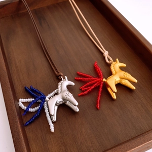 Detail of silver and gold horse pendant necklaces with colorful beaded tails on wood