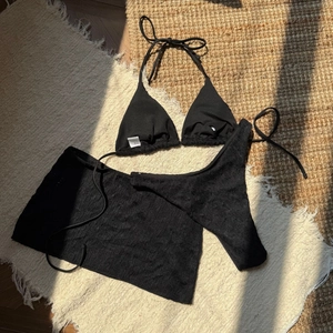 Detailed view of black three-piece bikini set with ribbed texture and lace mini skirt