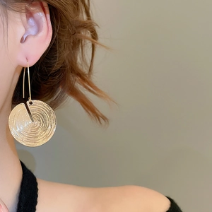 Close-up of a model wearing gold textured circular drop earrings with spiral pattern