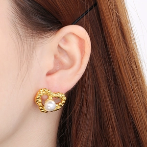 Macro detail of heart-shaped gold earring with textured edges and a white pearl bead