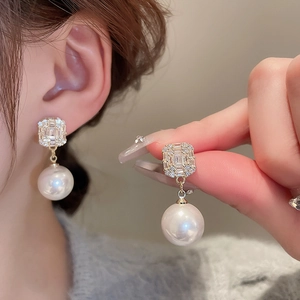Détail de boucles d'oreilles dorées avec zircons carrés et pendentifs en perles rondes