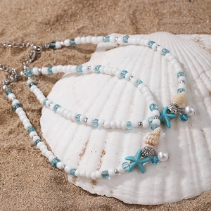 Detailed view of beach anklets with starfish and shell charms on white sand