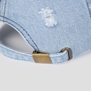 Close-up of adjustable bronze metal buckle on distressed light blue denim baseball cap
